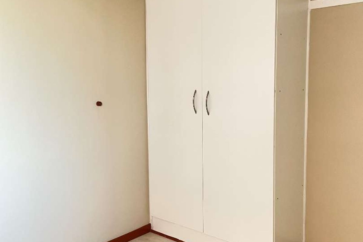 A simple bedroom featuring neutral wall tones, tiled flooring, and a white built-in wardrobe.