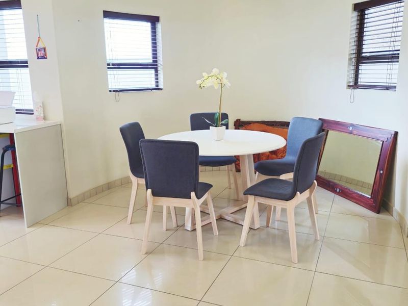 A bright dining area featuring large format floor tiles, a curved wall design, and multiple windows fitted with venetian blinds.
