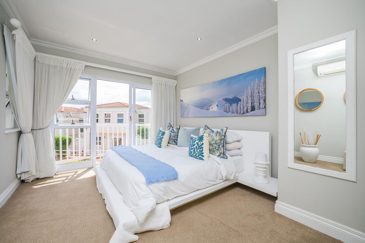 A bright and well-maintained bedroom featuring neutral carpeting, crown molding, recessed lighting, and sliding glass doors opening to a private balcony.