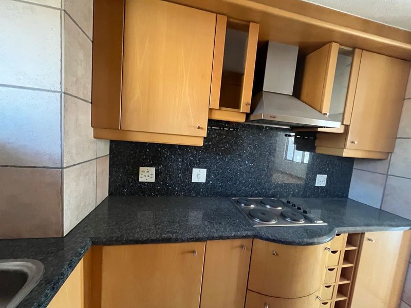 A functional kitchen featuring wooden cabinetry, granite countertops, a tiled backsplash, and a built-in electric hob with a stainless steel extractor fan.