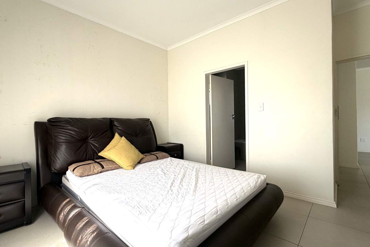 A bedroom featuring tiled flooring and neutral wall finishes, with an adjoining doorway leading to an en-suite bathroom.
