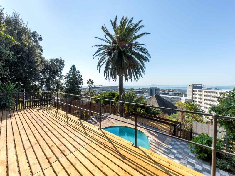 Elevated timber deck balcony overlooking a private swimming pool and paved patio area with expansive urban and coastal views.