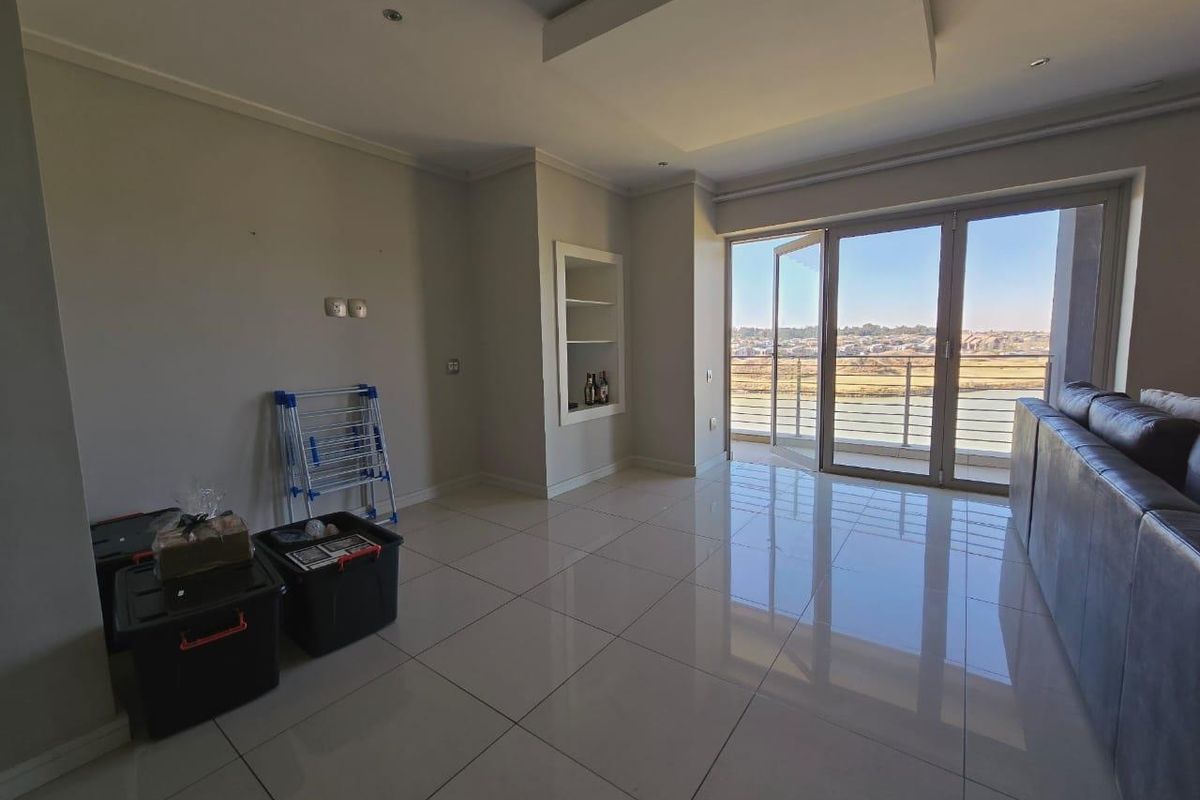 Spacious living area featuring large format floor tiles, recessed ceiling detail, built-in shelving, and expansive sliding glass doors leading to a balcony with views.