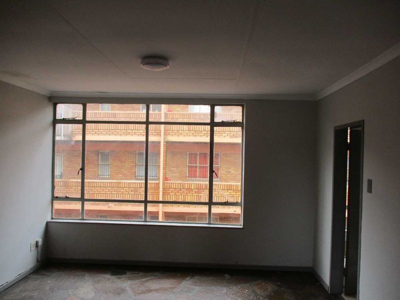 An empty living room featuring large steel-framed windows, stone flooring, and neutral walls, offering a blank canvas for interior design.