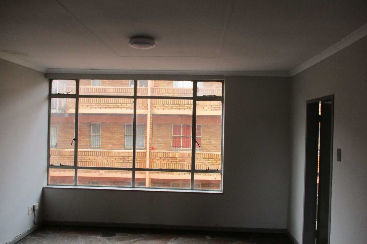 An empty living room featuring large steel-framed windows, stone flooring, and neutral walls, offering a blank canvas for interior design.