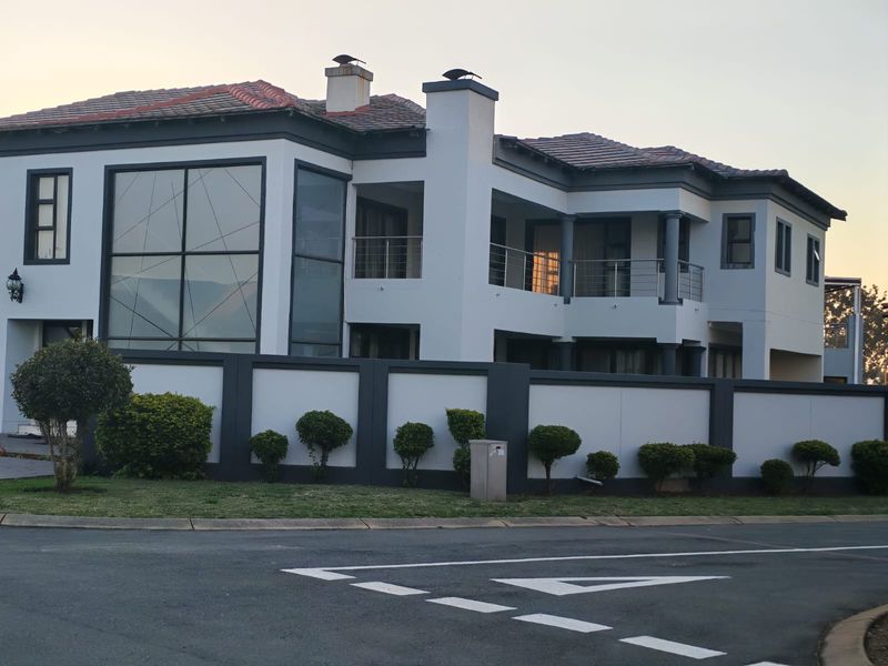 A modern two-story residential property featuring a tiled roof, large glass windows, and balconies, enclosed by a contemporary perimeter wall.