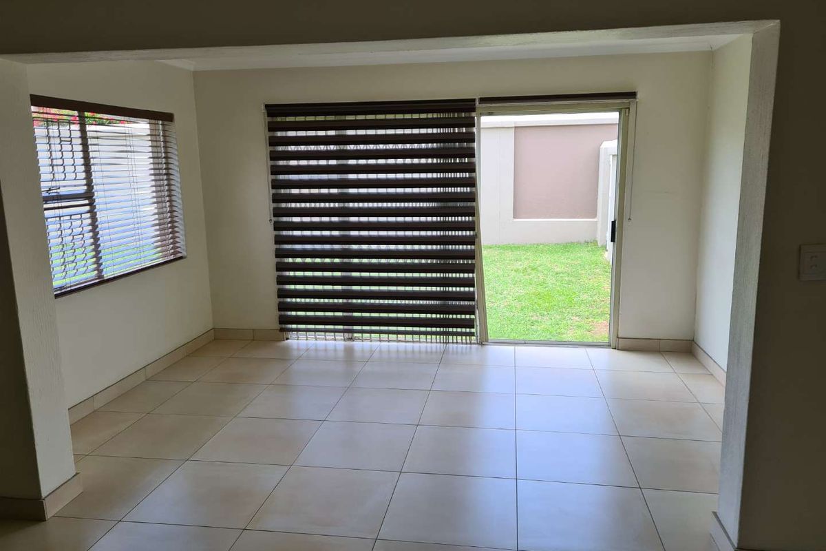 An empty living room featuring neutral tiled flooring, large sliding glass doors leading to the garden, and fitted window blinds.