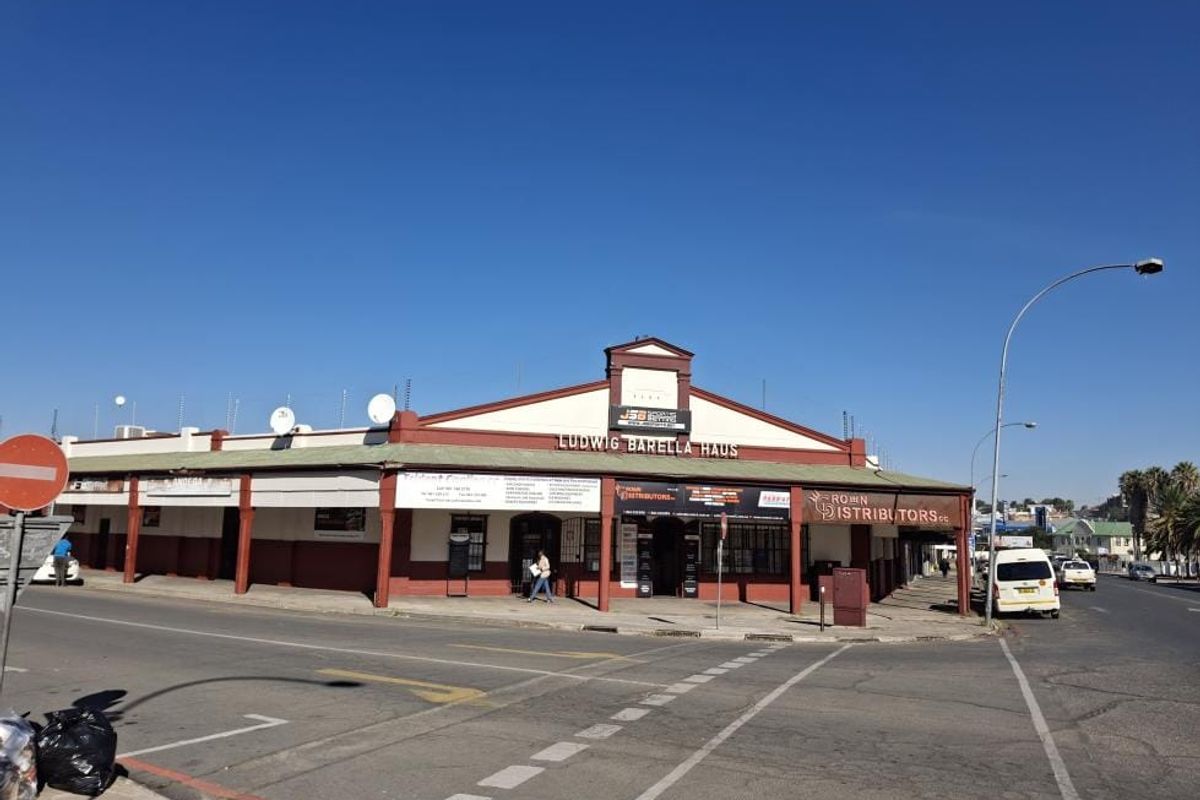 Street-level view of Ludwig Barella Haus, a commercial building featuring a covered walkway, prominent signage, and a corner-lot position.