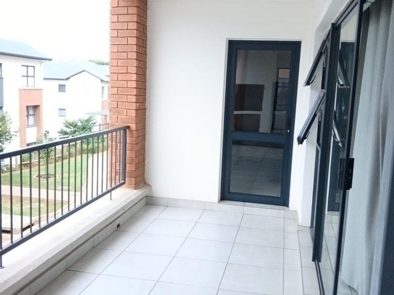 A clean, covered balcony featuring tiled flooring, a metal balustrade, and sliding glass door access to the interior living space.