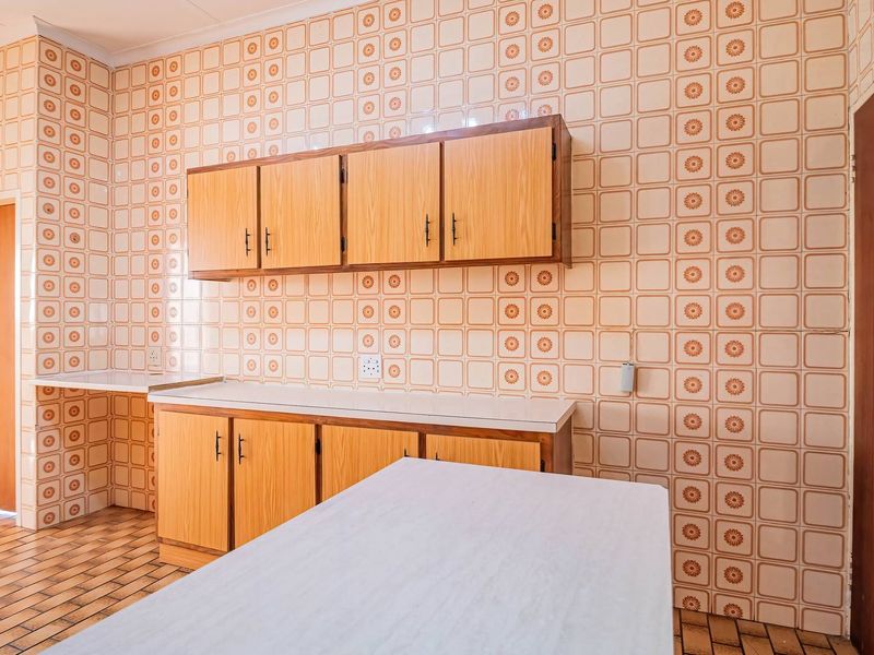 A dated kitchen featuring original patterned wall tiles, laminate cabinetry, and tiled flooring, offering a blank canvas for a modern renovation.