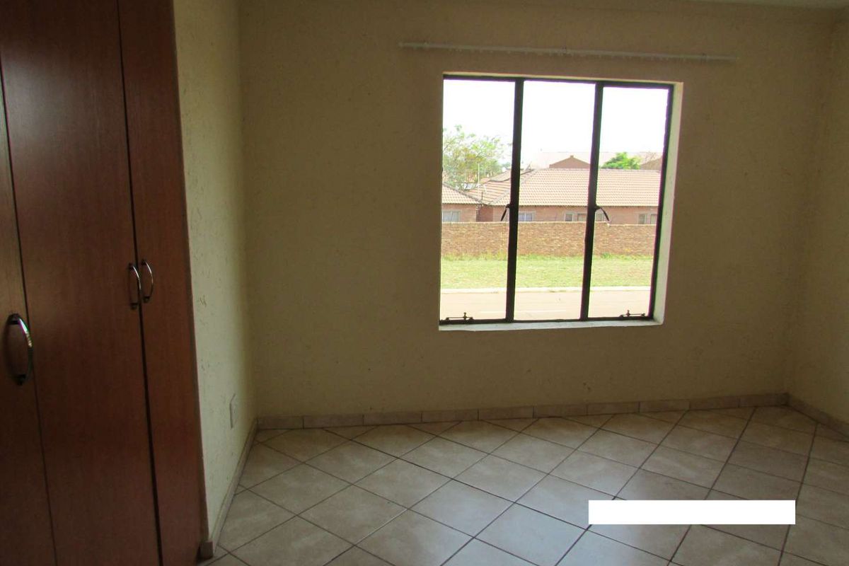 A vacant bedroom featuring tiled flooring, a built-in wardrobe, and a window with views of the surrounding neighborhood.
