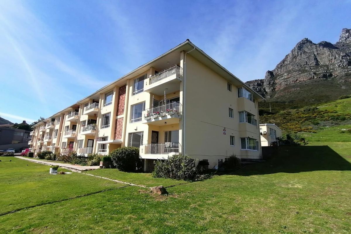 Exterior view of a multi-story apartment building featuring private balconies, set against a mountain backdrop with surrounding lawn areas.