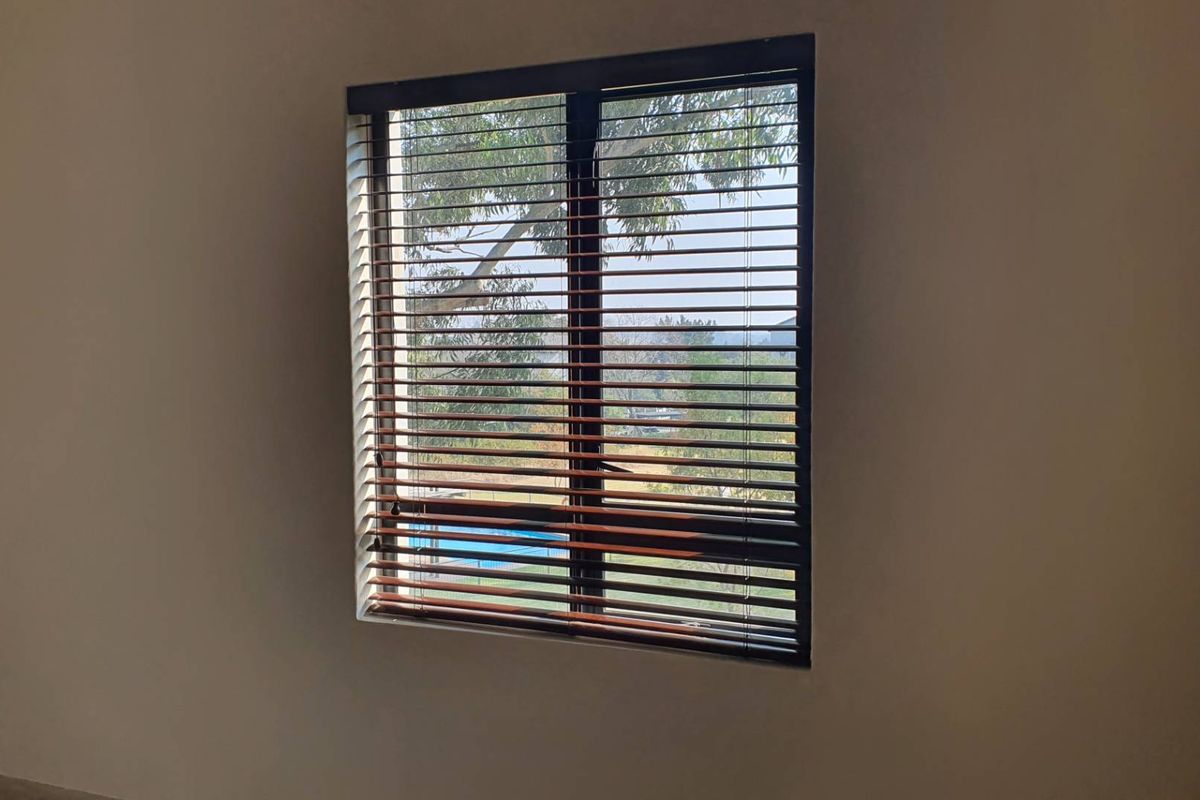 A bedroom interior featuring a window with installed wooden venetian blinds, offering a view of the outdoor area.