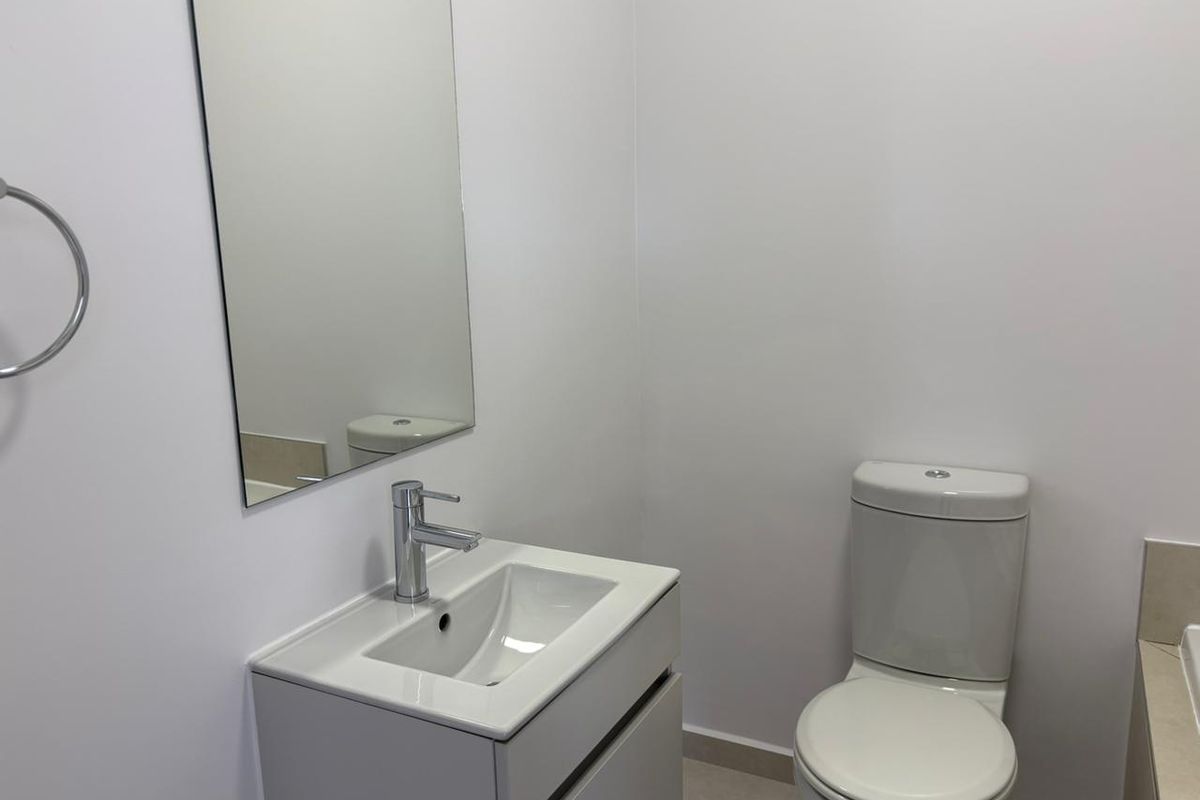 A clean and modern bathroom featuring a vanity with basin, wall-mounted mirror, and a standard toilet.