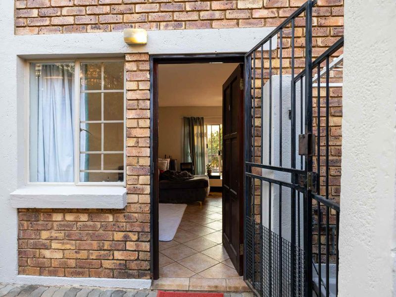 Exterior view of a townhouse entrance featuring a security gate, brick facade, and tiled flooring leading into the interior living space.