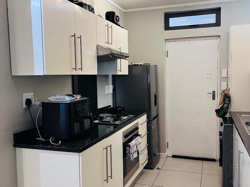 A functional kitchen featuring white cabinetry, black granite countertops, a gas hob, an electric oven, and tiled flooring with direct exterior access.
