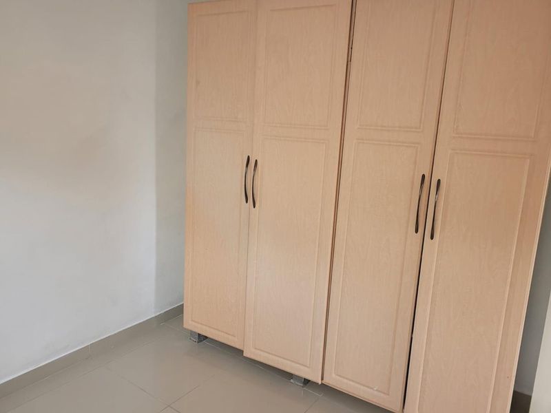 A bedroom featuring light wood-toned built-in wardrobes and neutral tiled flooring, offering a clean and functional storage solution.