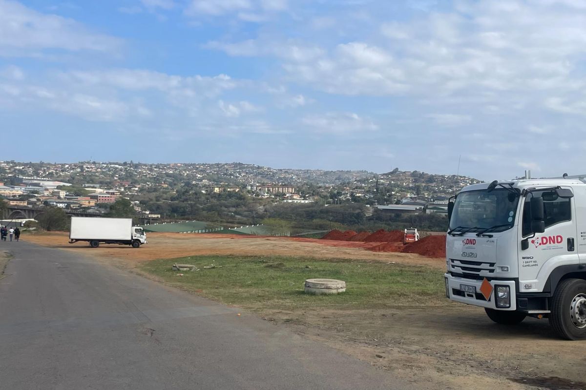 A view of a vacant commercial land plot with an unpaved access road and surrounding landscape.
