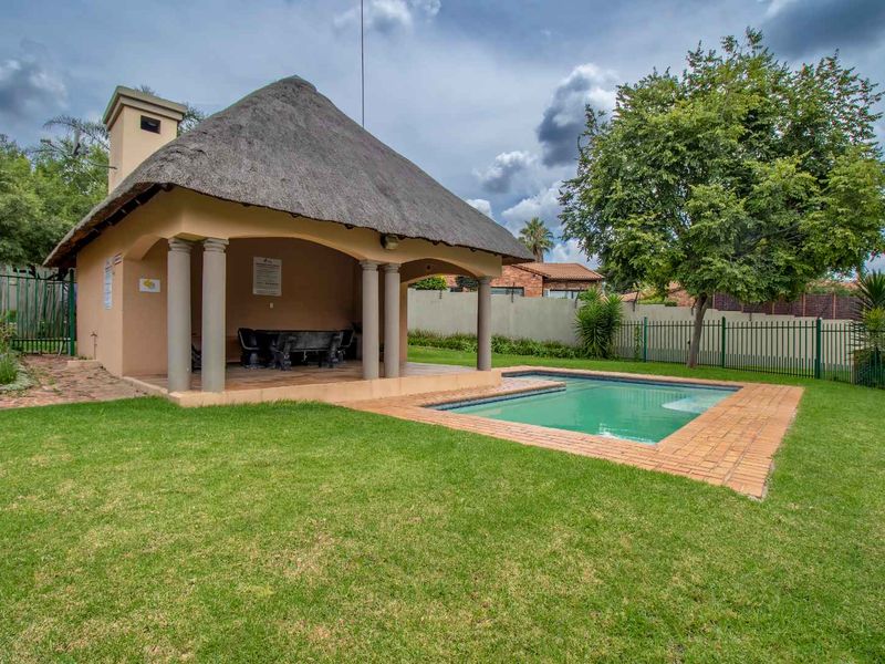 Outdoor entertainment area featuring a thatched roof lapa, swimming pool, and well-maintained garden space within a secure complex.