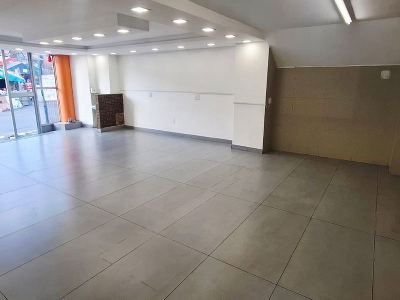 Spacious open-plan commercial unit featuring large glass storefront windows, recessed ceiling lighting, and durable tiled flooring, suitable for various business applications.