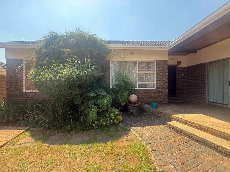 A rear exterior view of a brick house featuring a paved patio area, sliding glass doors, and established garden landscaping.