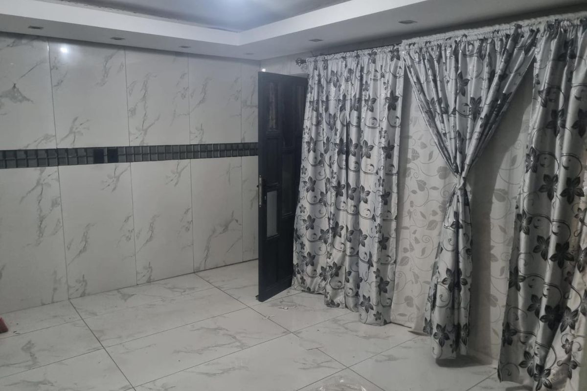 An empty living area featuring marble-look wall and floor tiles, recessed ceiling lighting, and a drop ceiling design.