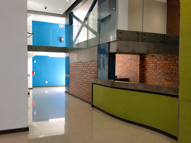 Modern commercial-style entrance lobby featuring a reception desk, exposed brickwork, glass balustrades, and polished tiled flooring in a contemporary open-plan layout.