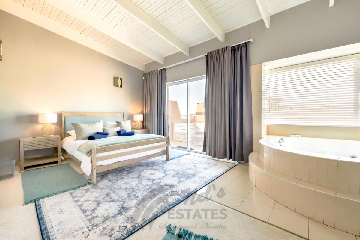 Spacious bedroom featuring a built-in circular bathtub, vaulted timber ceiling, and sliding glass doors leading to a private balcony.