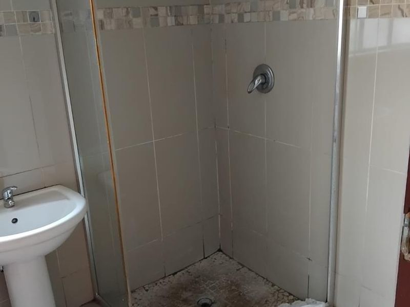 A compact bathroom featuring a pedestal basin and a corner shower enclosure with tiled finishes.