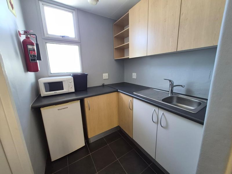A compact office kitchenette featuring built-in cabinetry, a stainless steel sink, laminate countertops, and tiled flooring.