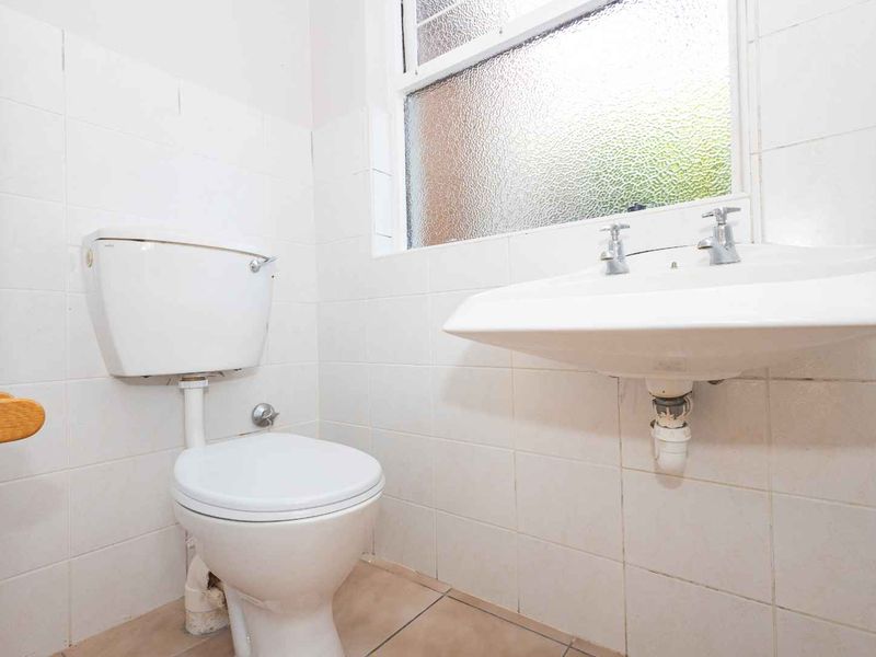A compact bathroom featuring a wall-mounted basin, ceramic toilet, and tiled finishes, requiring cosmetic updates to modernize the space.