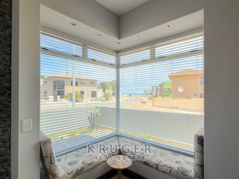 A bright living area featuring a corner window with built-in seating, recessed lighting, and a modern stone feature wall.