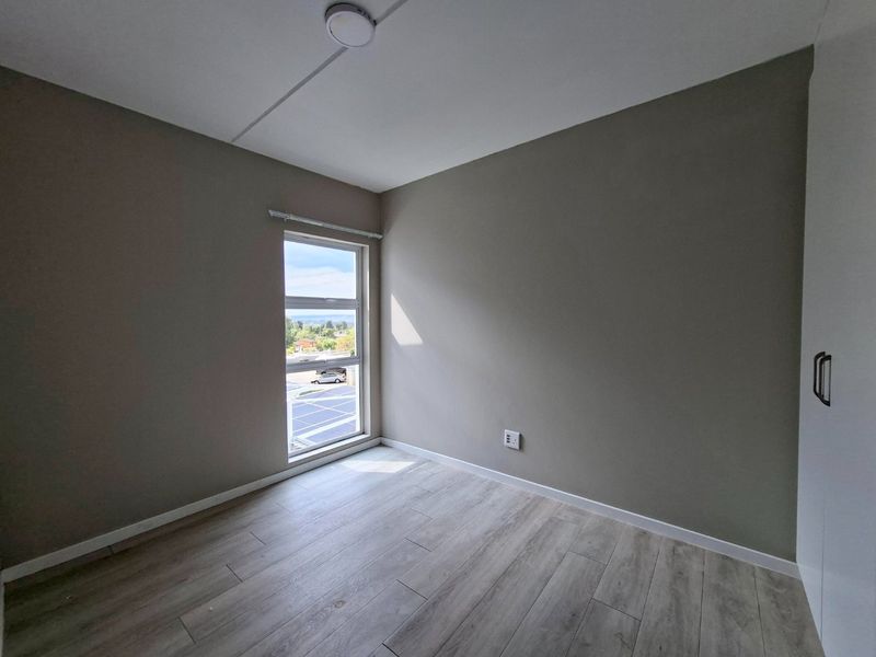A bright, empty bedroom featuring modern laminate flooring, neutral walls, and a built-in cupboard with a view through the window.