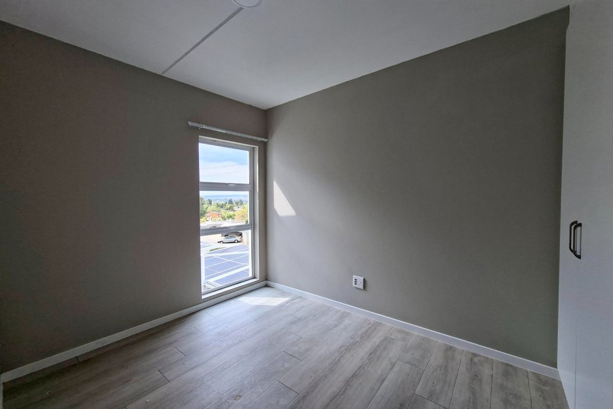 A bright, empty bedroom featuring modern laminate flooring, neutral walls, and a built-in cupboard with a view through the window.