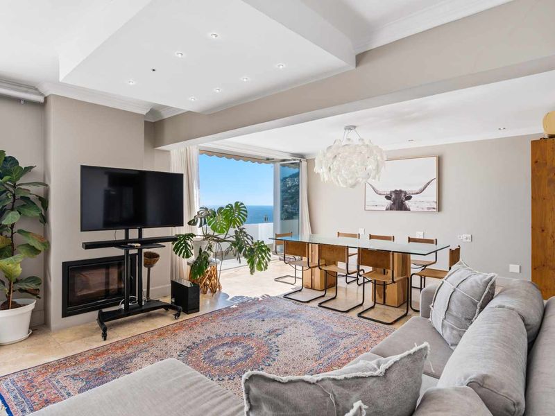 Spacious open-plan living and dining area featuring stone flooring, a built-in fireplace, recessed ceiling lighting, and seamless access to a balcony with ocean views.