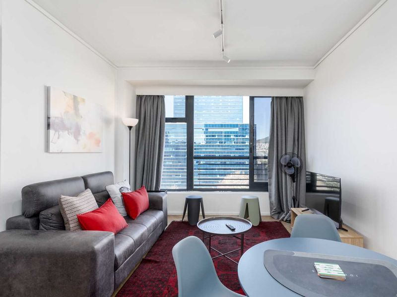 A bright open-plan living and dining area featuring large windows with city views and modern track lighting.