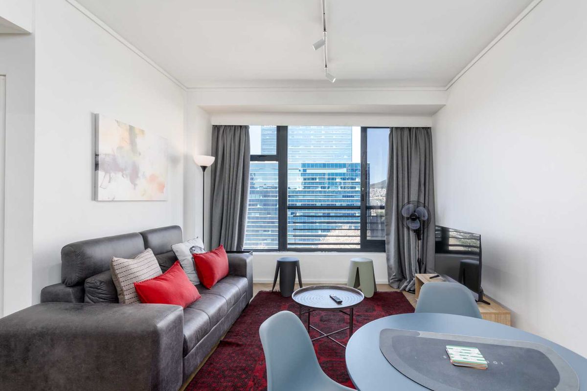 A bright open-plan living and dining area featuring large windows with city views and modern track lighting.