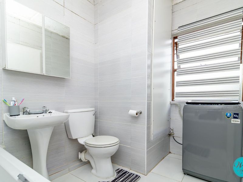 A functional bathroom featuring a pedestal basin, toilet, and full-height wall tiling, with a window providing natural light.