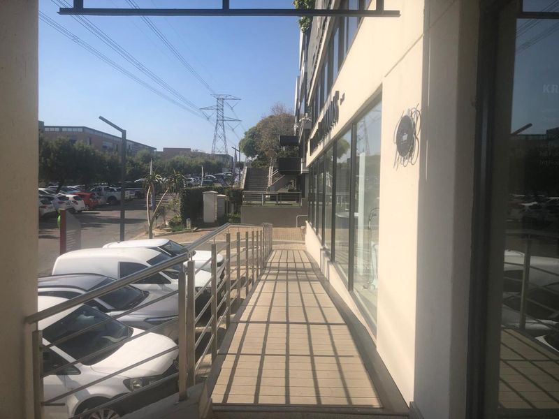 A view of the office building exterior featuring a paved walkway with a stainless steel handrail and large glass storefront windows.