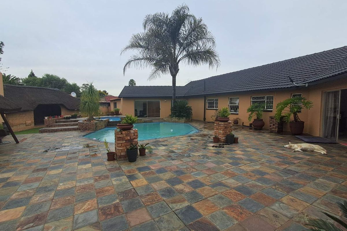 Spacious rear courtyard featuring a swimming pool, tiled patio area, and a thatched lapa structure, ideal for outdoor entertaining.