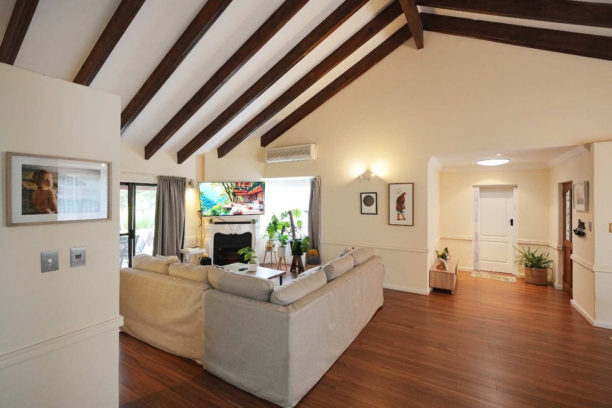 Spacious living room featuring high vaulted ceilings with exposed timber beams, wood-look flooring, a built-in fireplace, and split-system air conditioning.