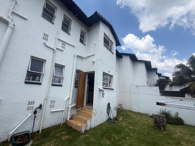 Rear view of a townhouse featuring a textured white facade, tiled entrance steps, and visible external plumbing with a small private garden area.