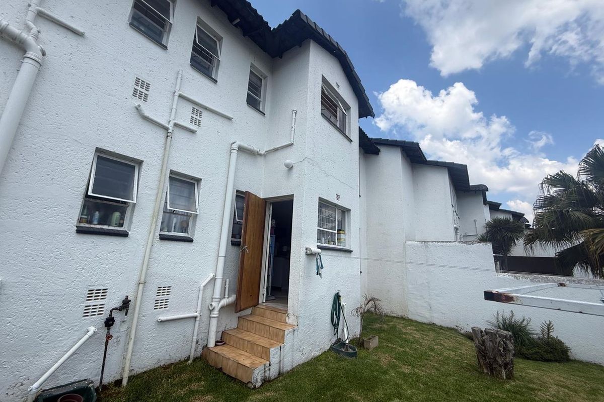 Rear view of a townhouse featuring a textured white facade, tiled entrance steps, and visible external plumbing with a small private garden area.