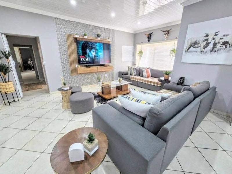 A well-maintained living room featuring tiled flooring, a decorative feature wall with integrated media unit, and recessed ceiling lighting.