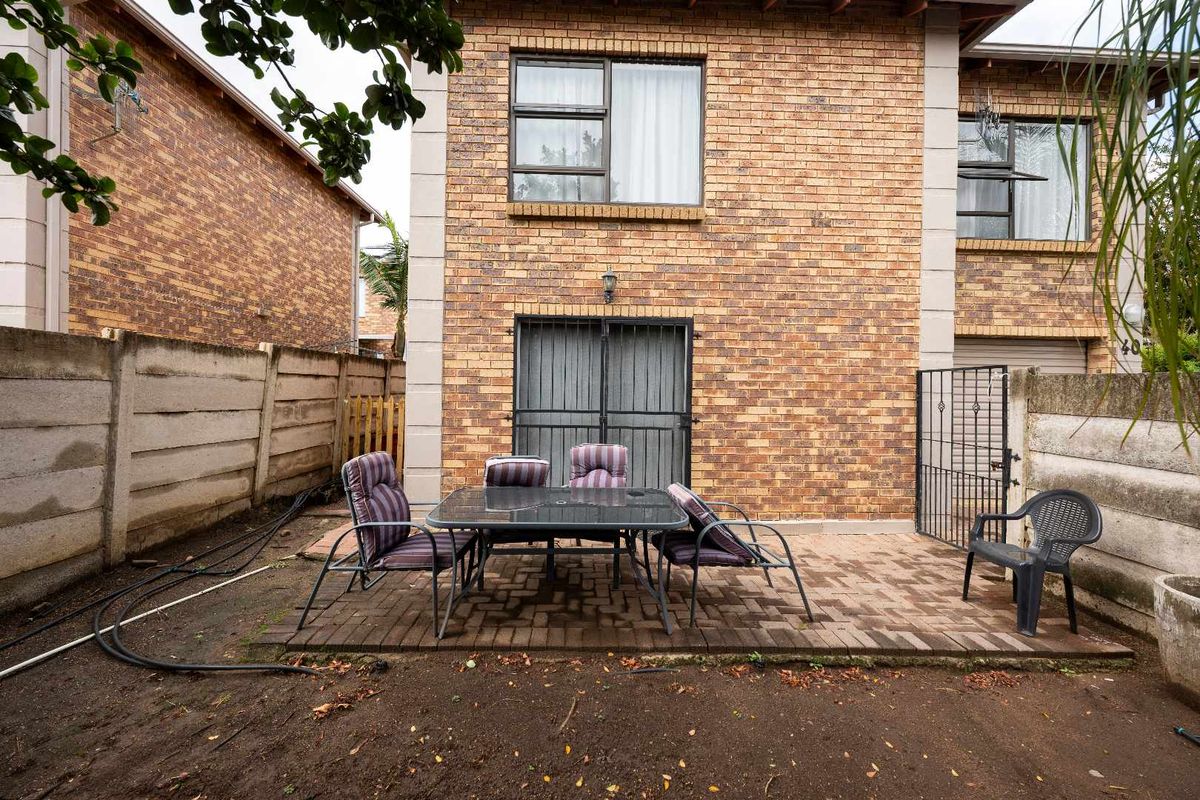 Rear view of the townhouse featuring a paved patio area, brick facade, and a private garden space enclosed by boundary walls.