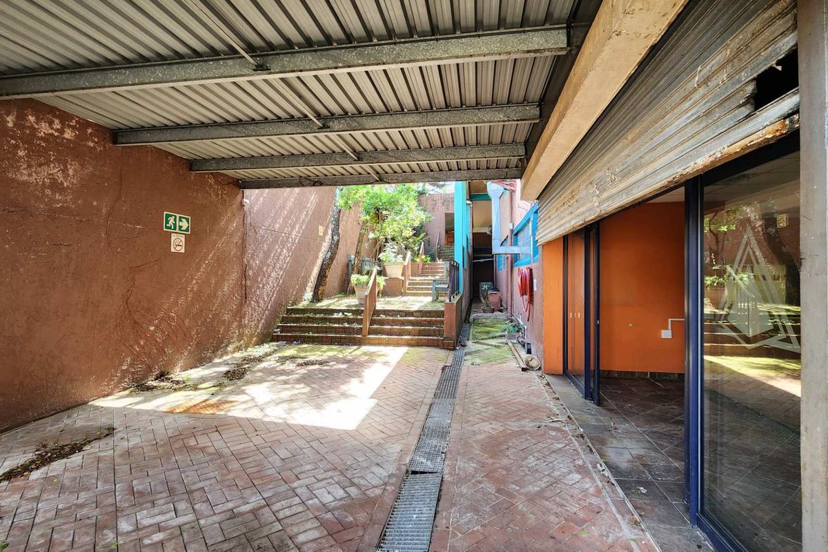 Covered outdoor retail access area featuring paved flooring, a metal roof structure, and a roller shutter door entrance.