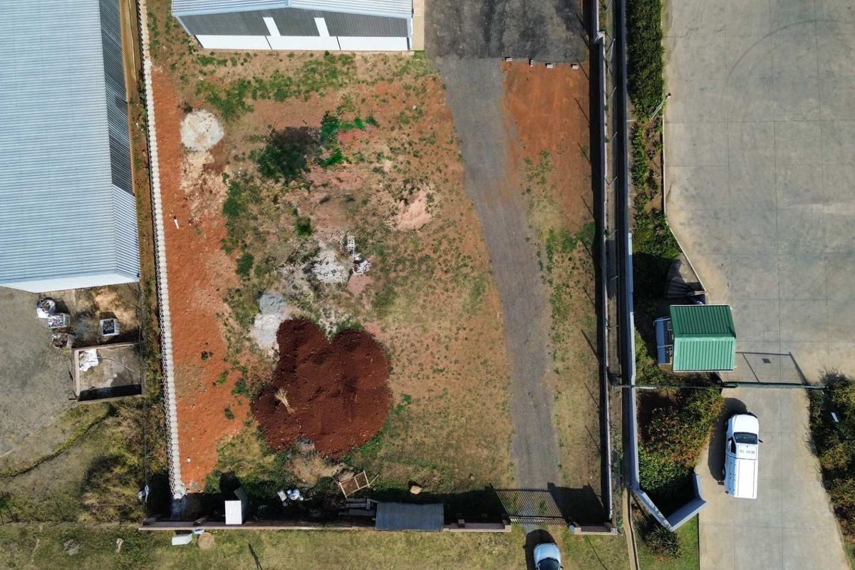 Aerial view of a vacant commercial plot featuring perimeter fencing, a security guard house, and an existing gravel driveway access point.