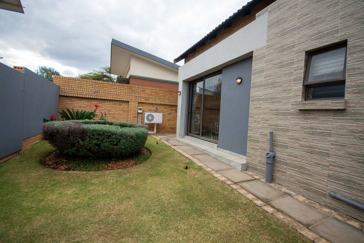 A well-maintained rear garden featuring a paved walkway, sliding glass doors, and a brick boundary wall.