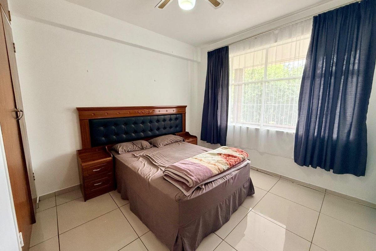 A bedroom featuring large format floor tiles, a ceiling fan, and a window with security bars and curtains.