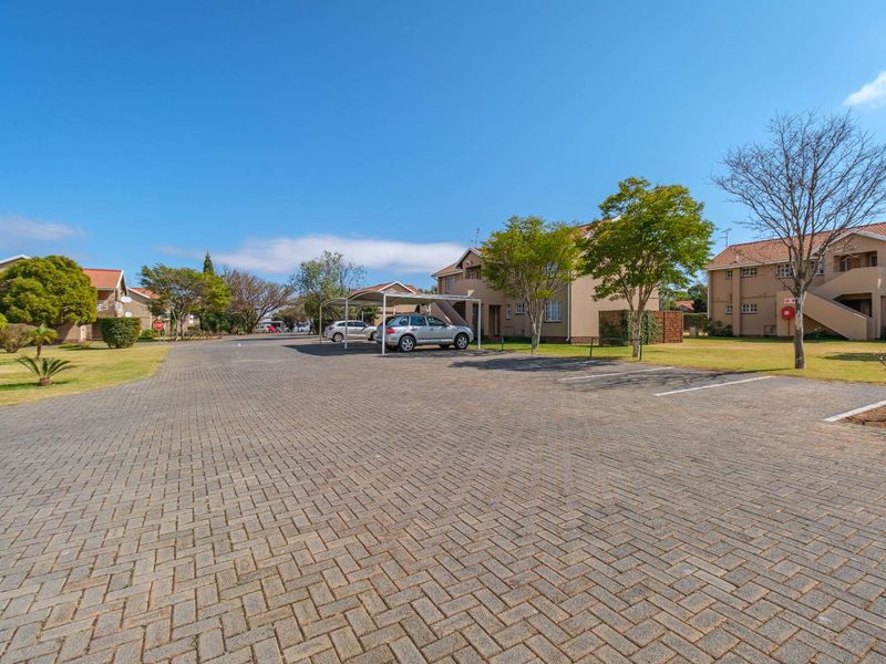 Exterior view of an apartment complex featuring a paved parking area, covered carports, and well-maintained communal garden spaces.